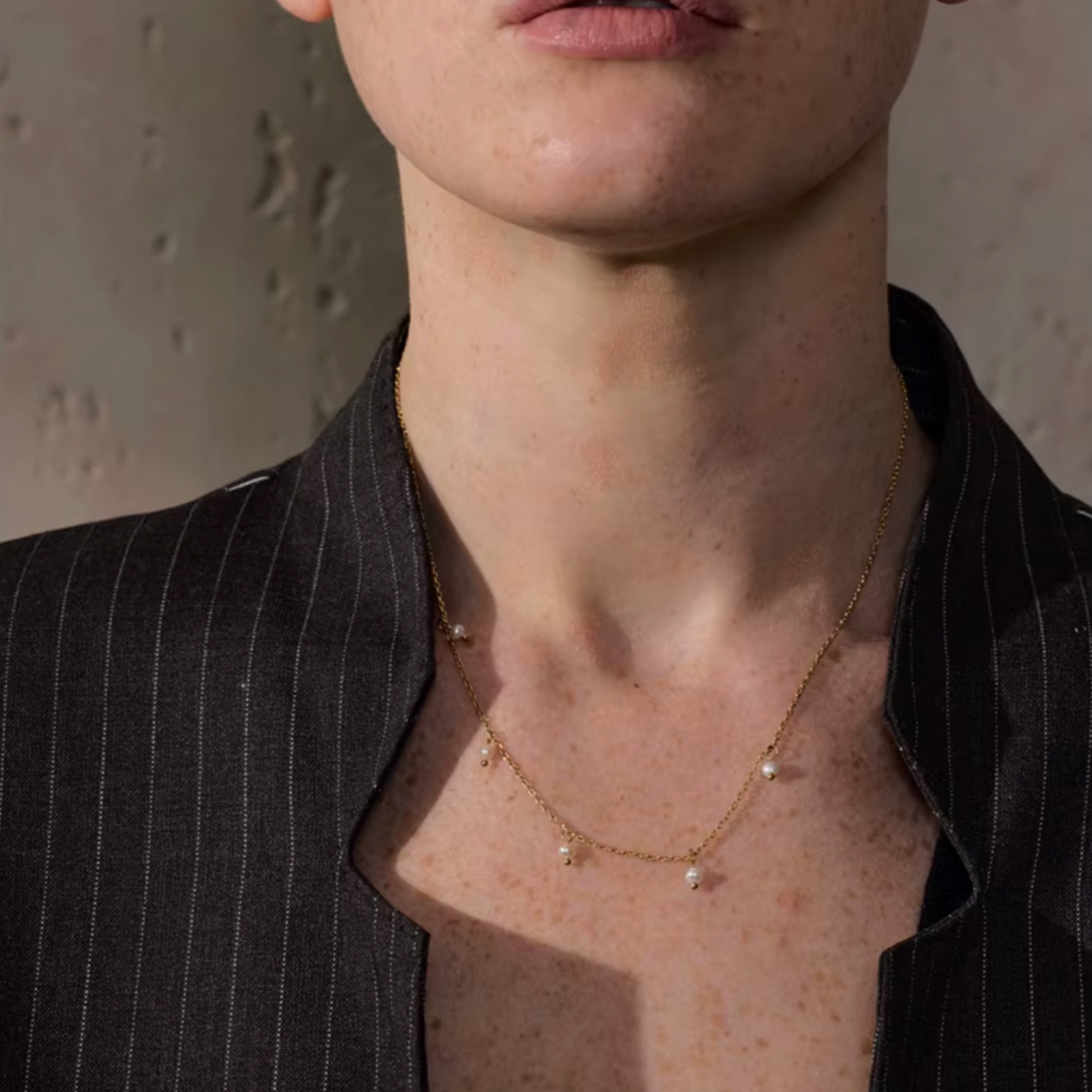 Close-up of a person wearing a gold necklace with small pendants against a neutral background
